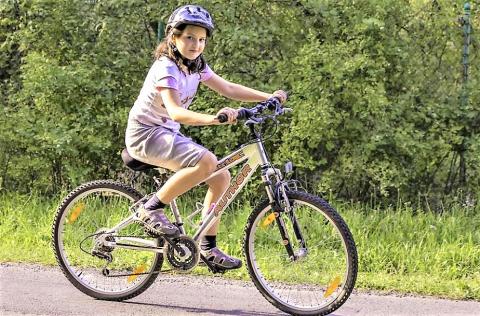 Girl with helmet, riding a bike in a park.