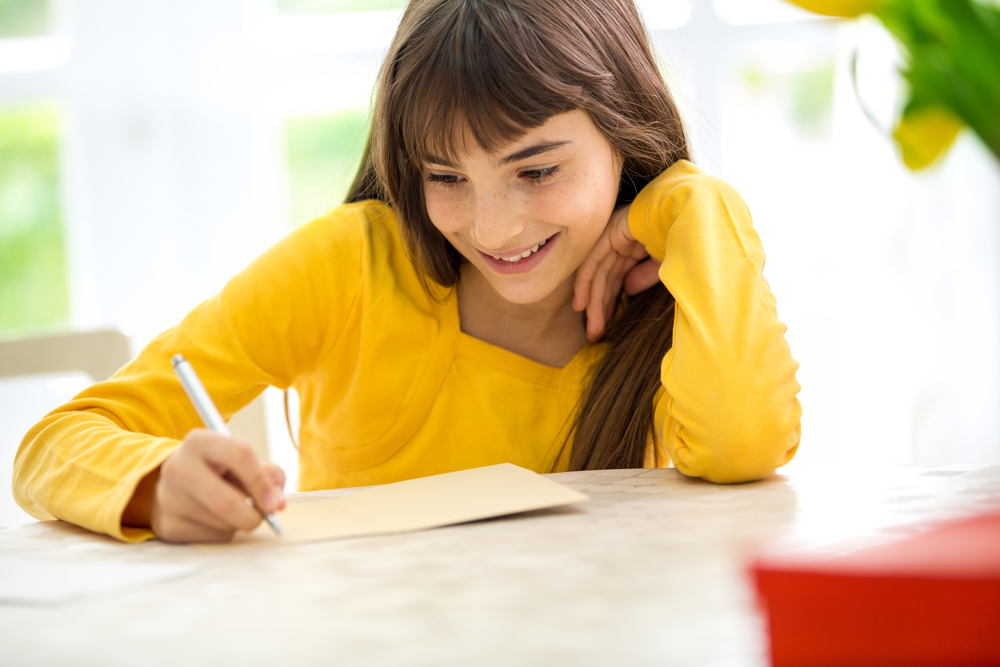 School age girl wearing a yellow shirt and writing.