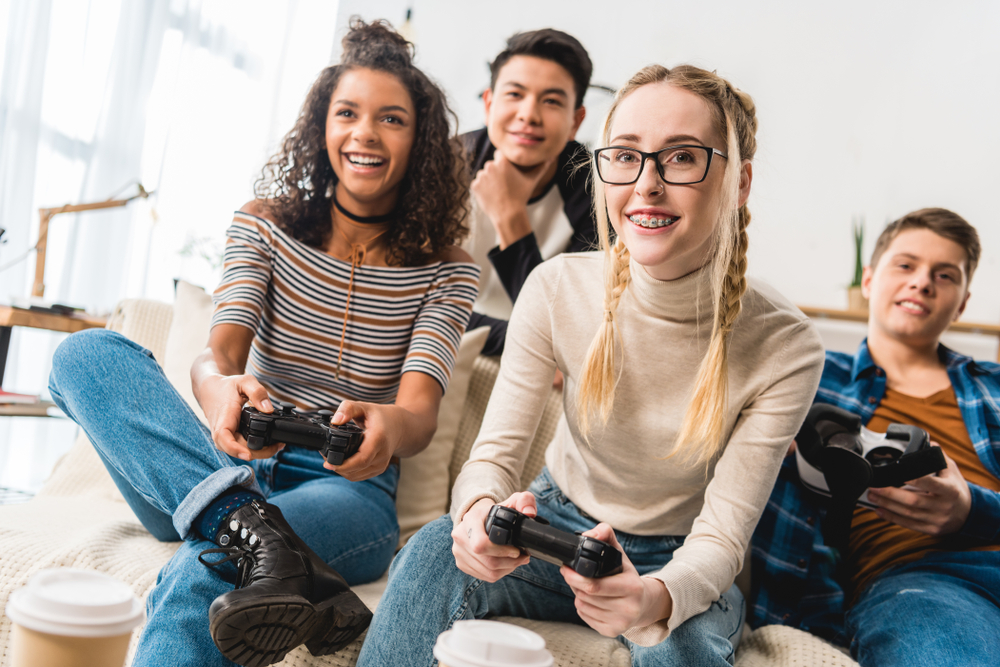 Two teenage girls and two teenage boys playing video games together.