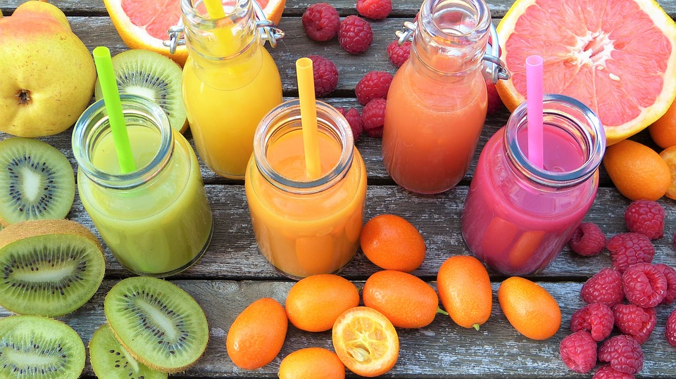 Green, orange, and pink smoothies in mason jars surrounded by fruit.