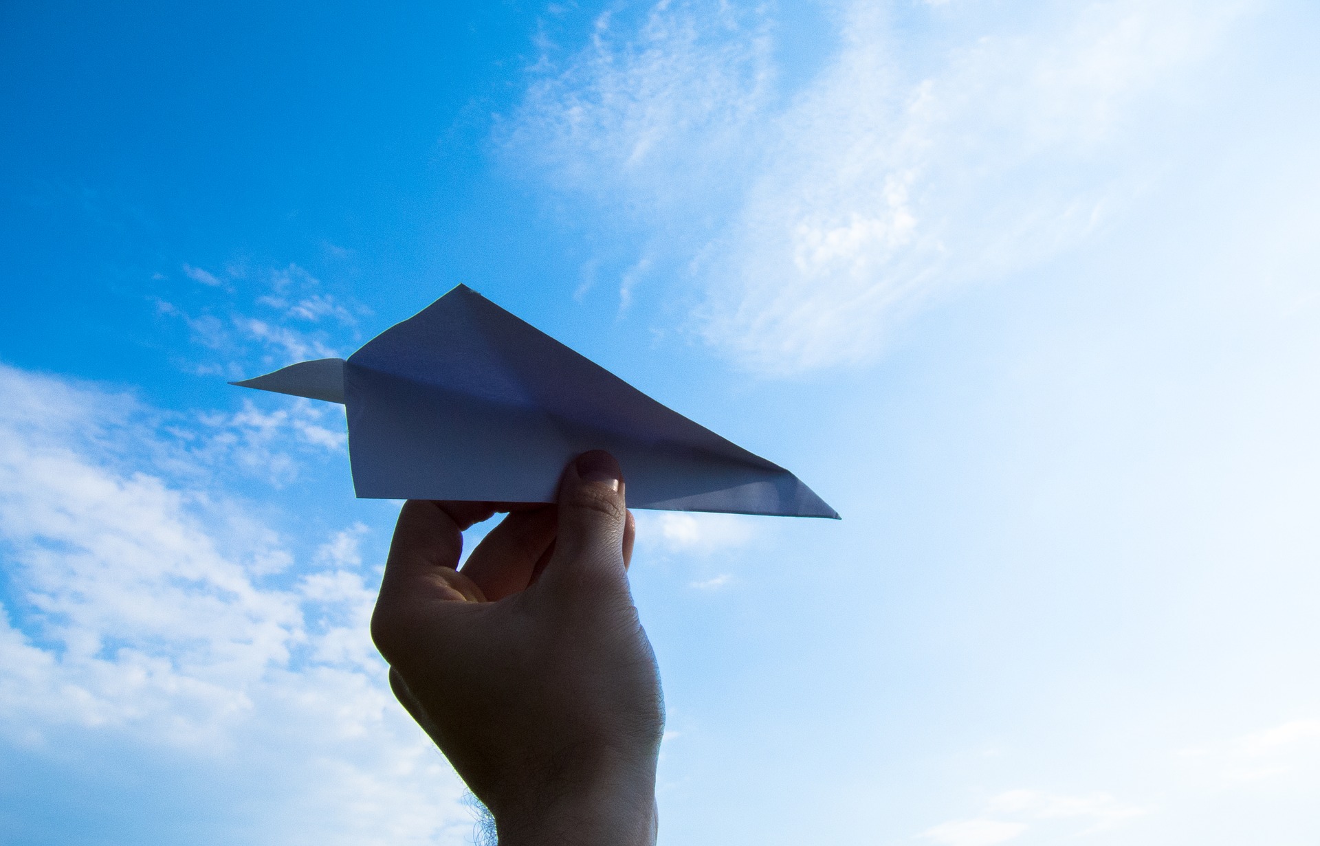 Hand holding a paper airplane into the sky