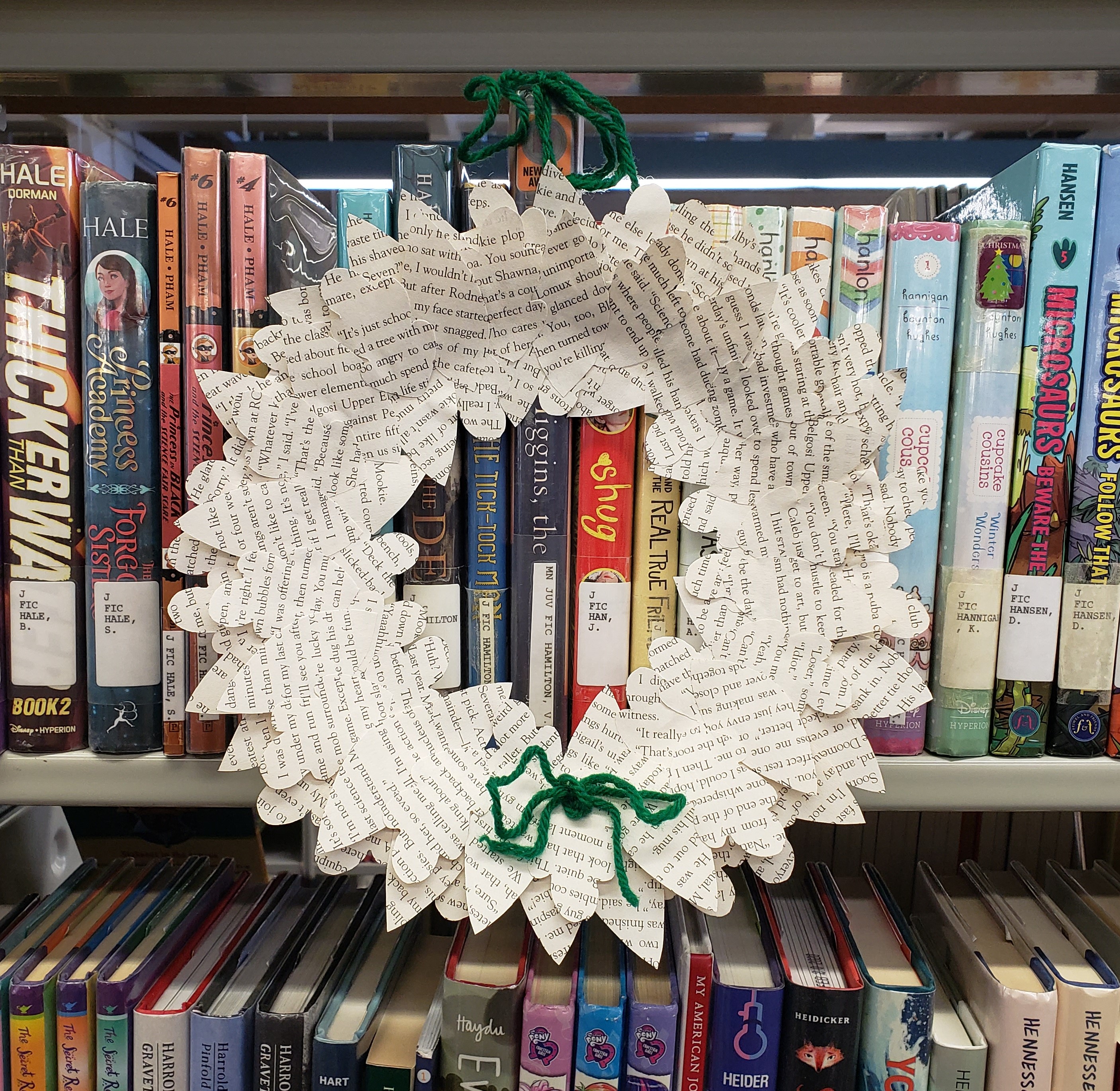 Wreath with leaves made from old book pages hanging off bookshelf