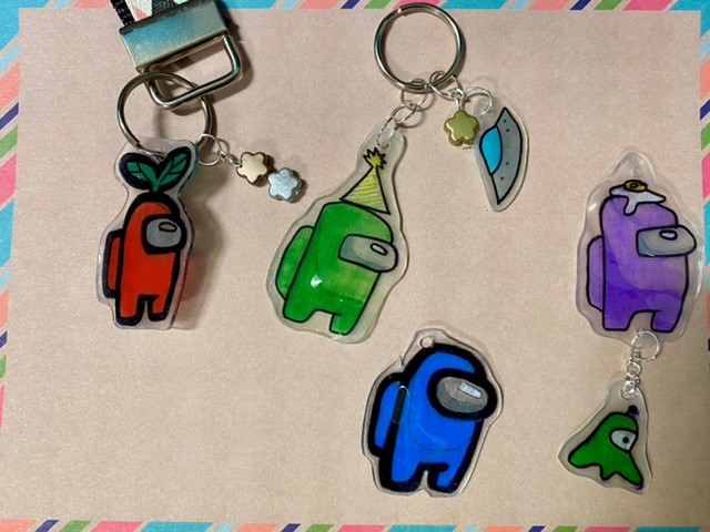 Among Us crewmate keychains, Red, Green, Blue and purple with a tan background.