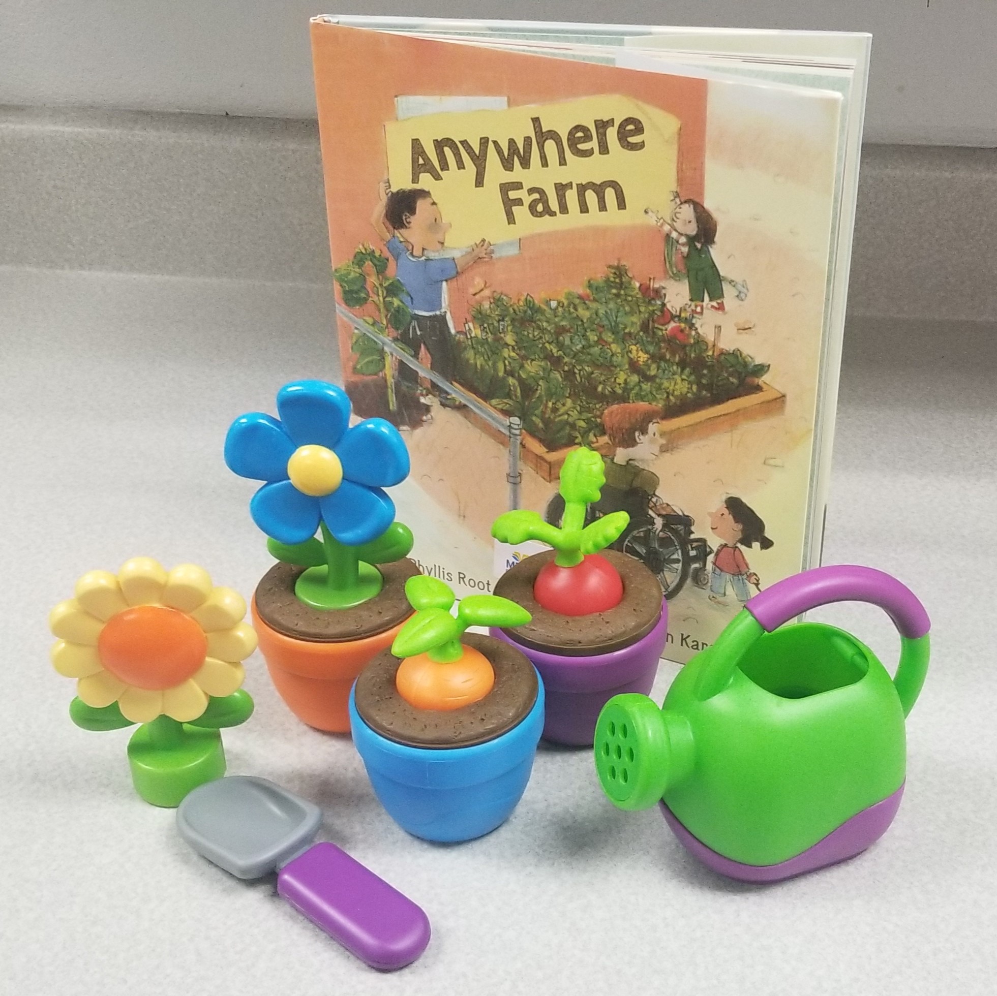 Image of playset including a watering can, plants, and trowel and a book titled "Anywhere Farm"
