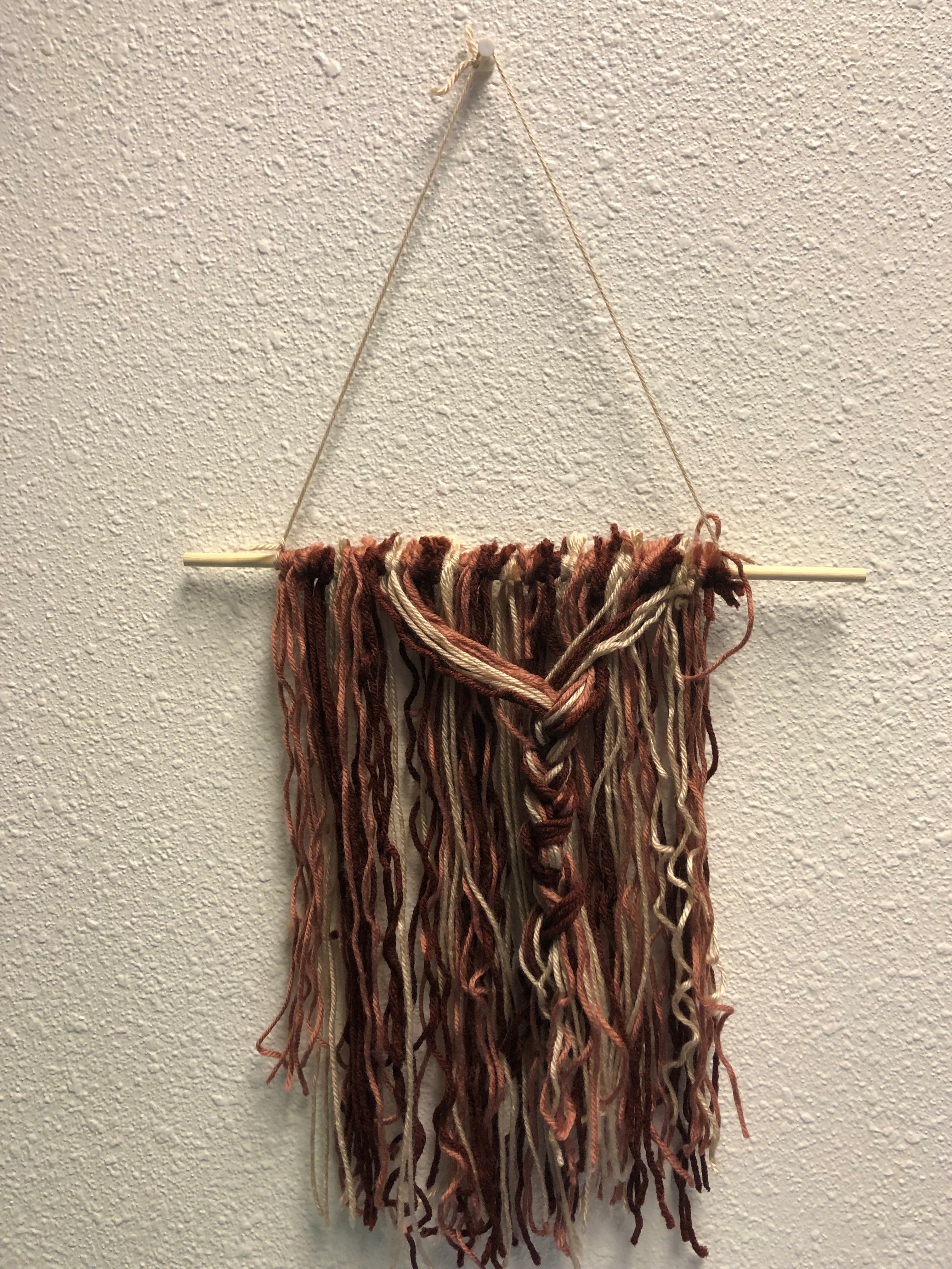 Rust, coral, and beige yarn hanging with braid in middle