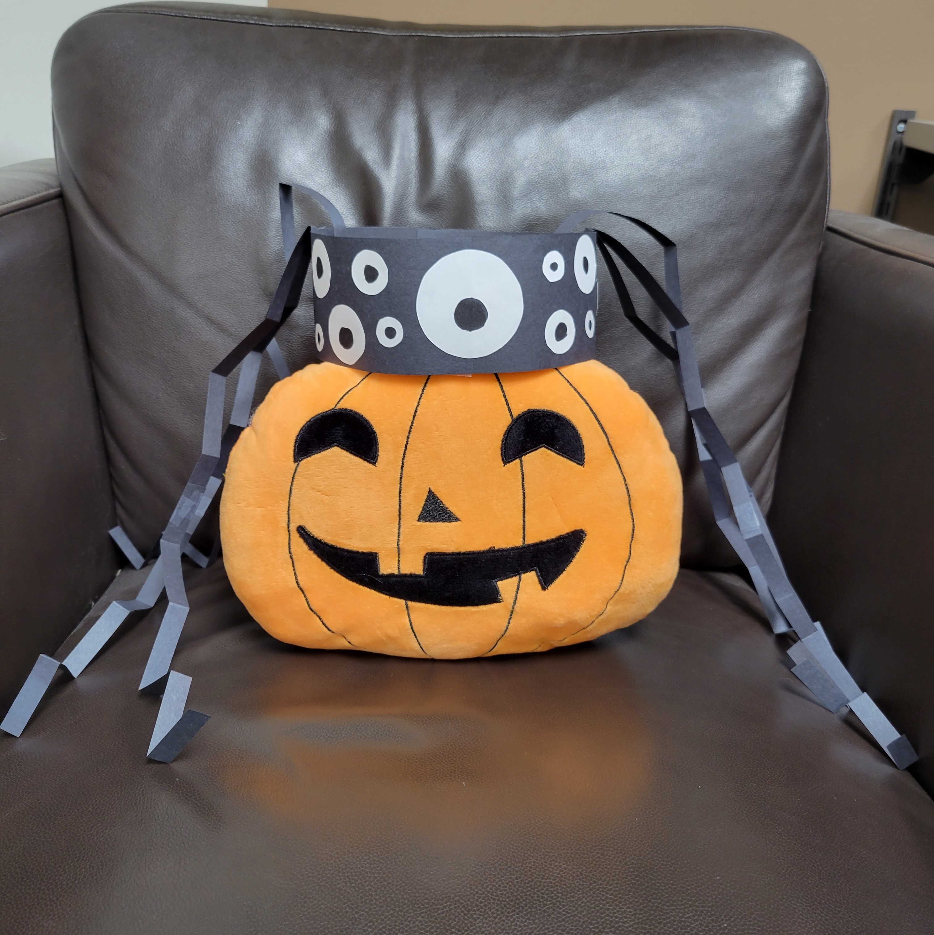paper spider headband sitting on top of plush jack-o-lantern sitting in a leather chair