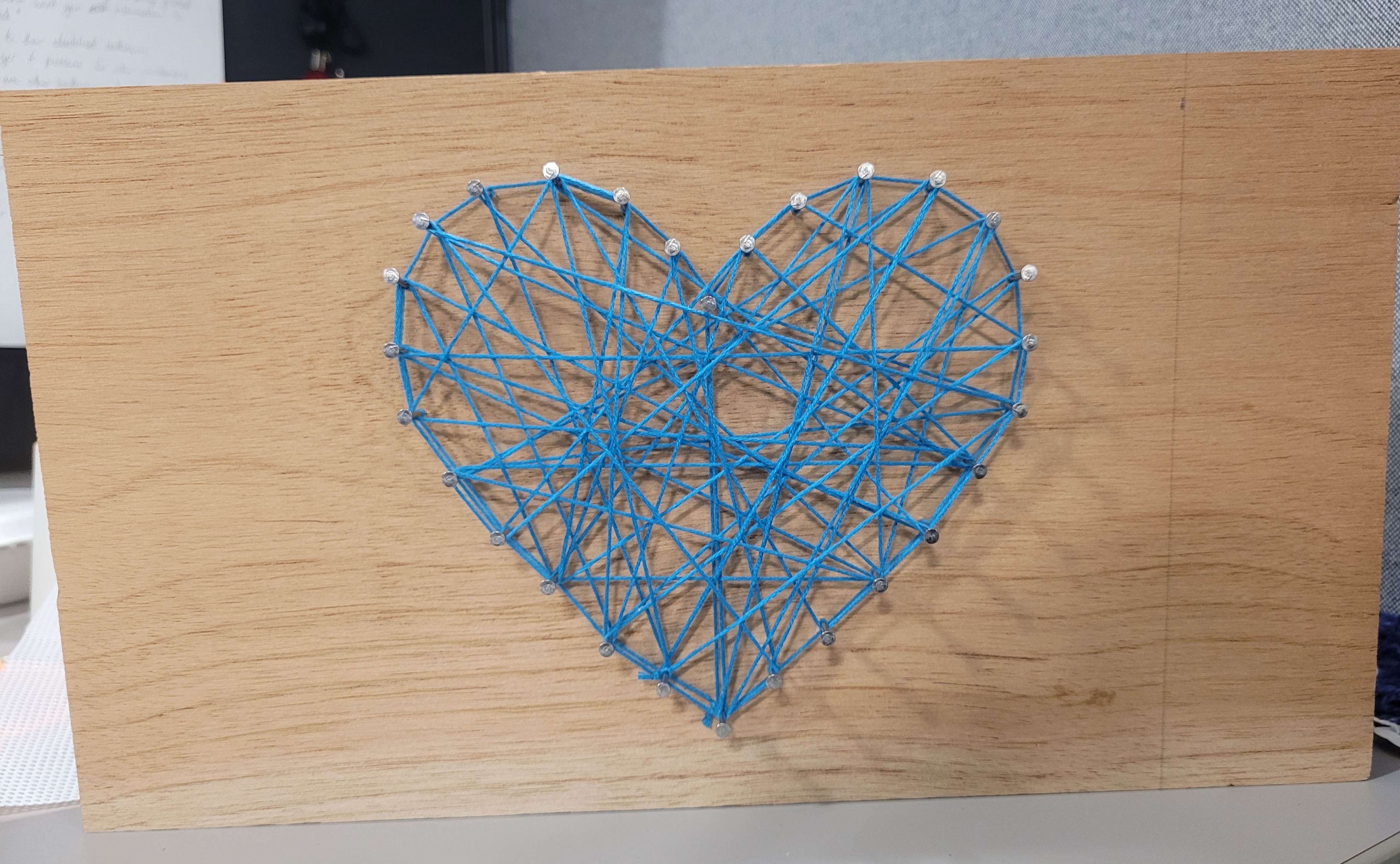 wood board with small, silver nails and blue embroidery floss making a heart