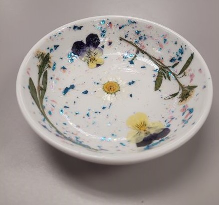 palm-sized white, porcelain dish with dried, pressed flowers and glitter paint.