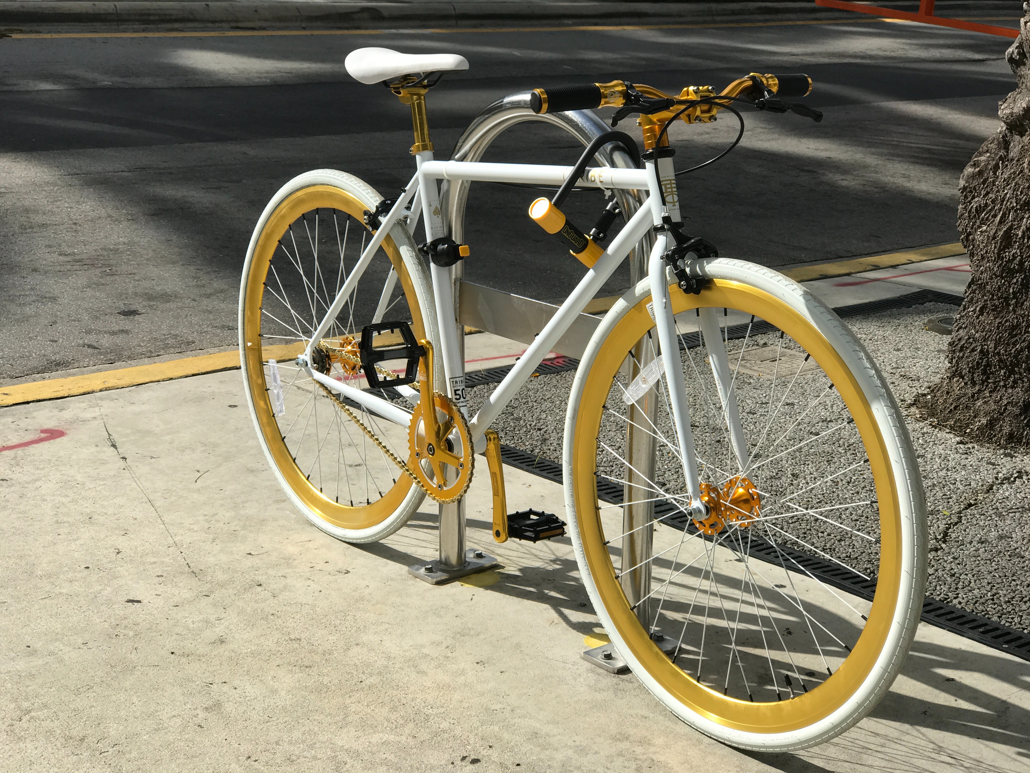 White bicycle chained to a bike rack along a street
