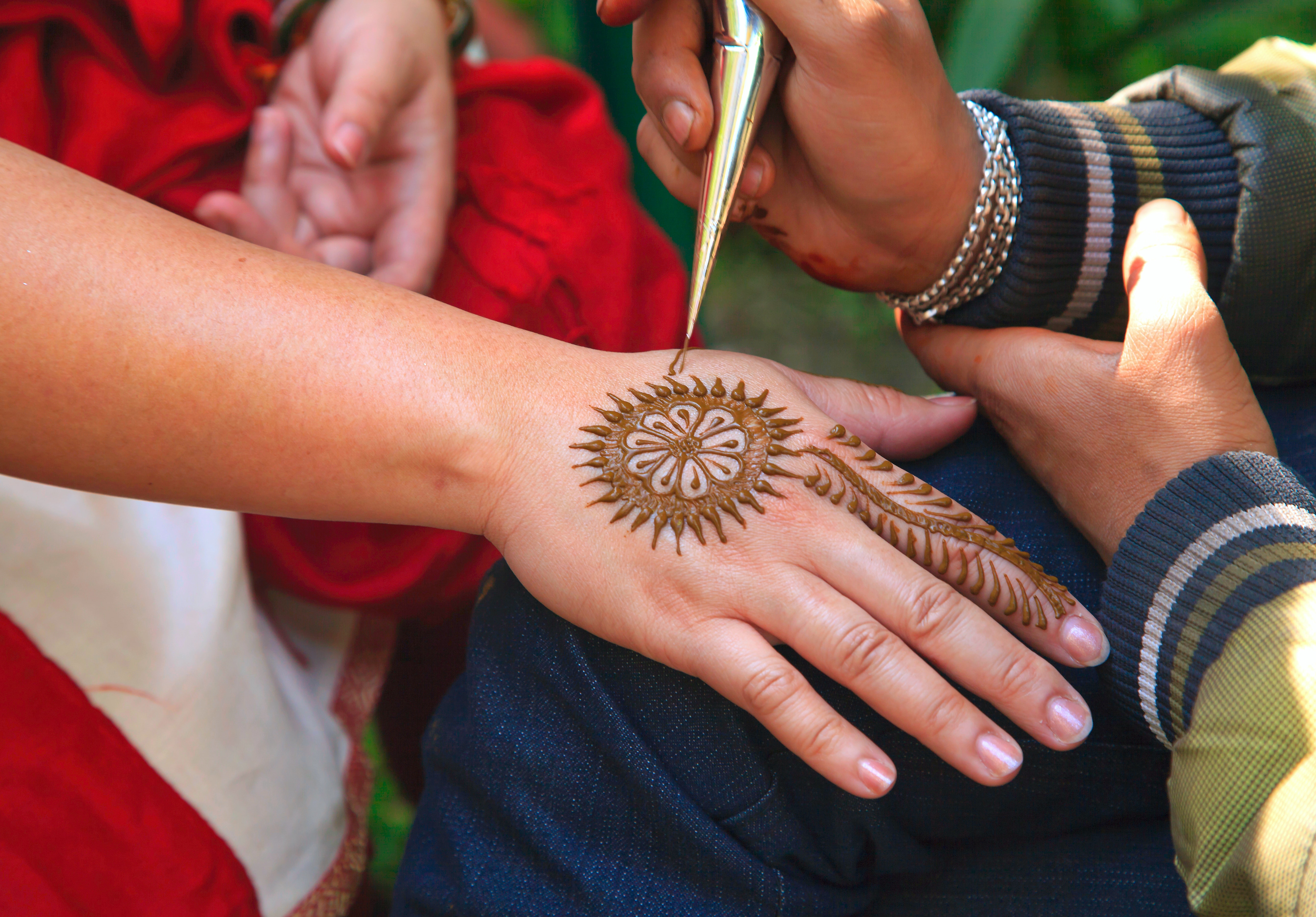 Artist drawing mehendi designs in henna on another's hands