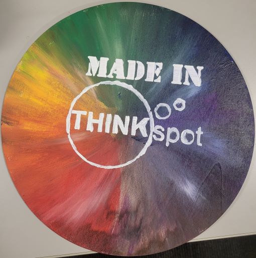 unfinished wood circle painted in red, orange, yellow, green, blue, purple, brown, silver with white streaks.  Made in THINKspot logo in center.