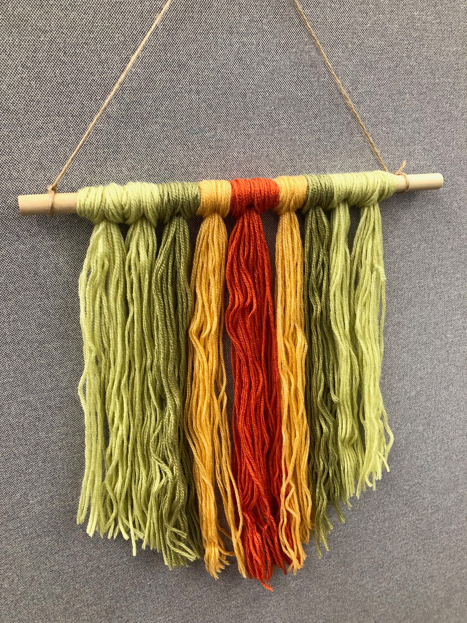 wooden dowel with green, yellow, orange yarn tied to it