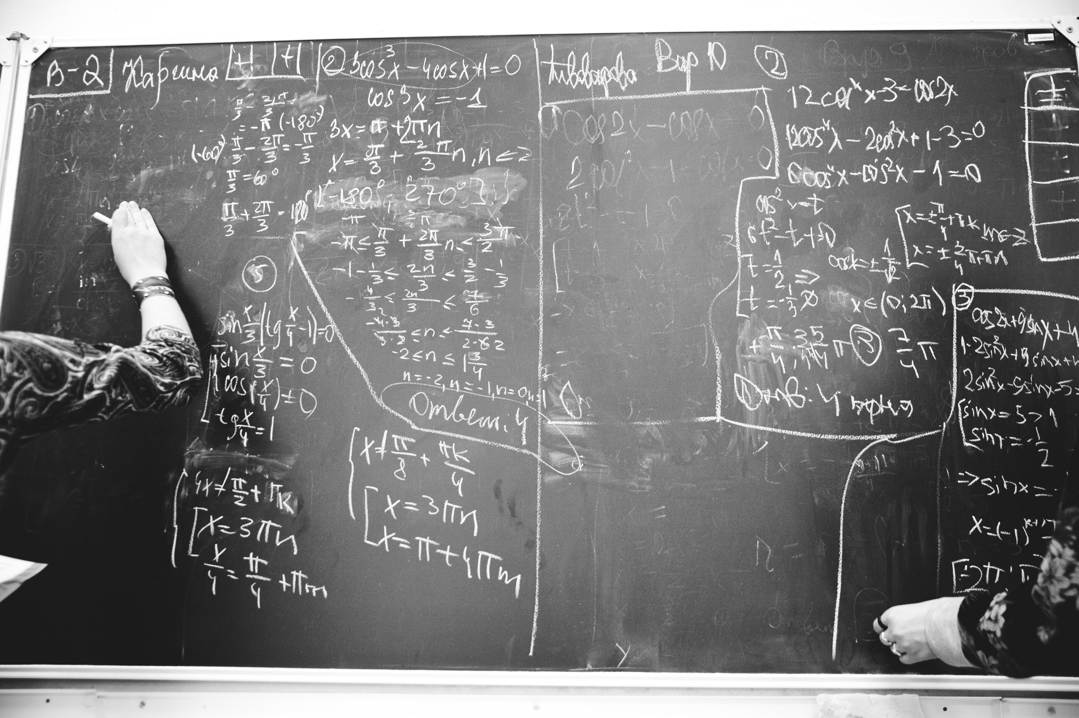Teacher at blackboard, writing out math equations.
