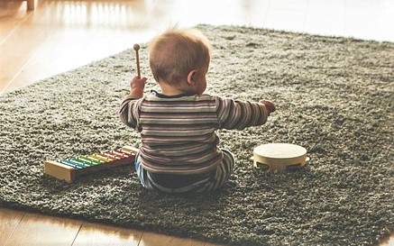 Baby sitting on carpet playing with a toy xylophone and tamborine