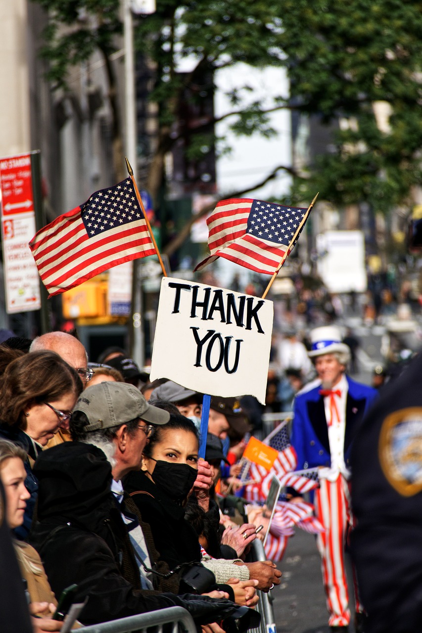 Veterans Day street parade with people holding thank you signs.  Uncle Sam is also walking in the parade.   
