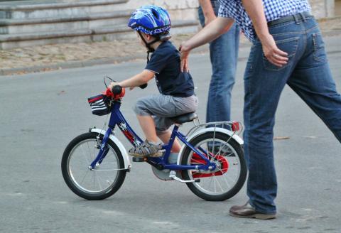 Young child learning to ride a bicycle and wearing a helmet.