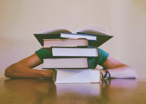 College student behind a pile of books on a desk.