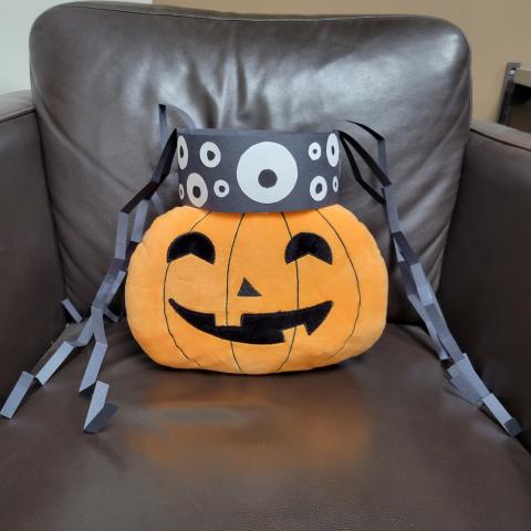 paper spider headband sitting on top of plush jack-o-lantern sitting in a leather chair