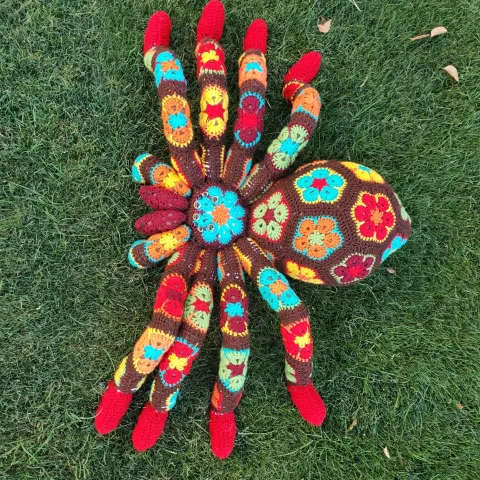 Crocheted multicolored, mostly red spider on grassy background.