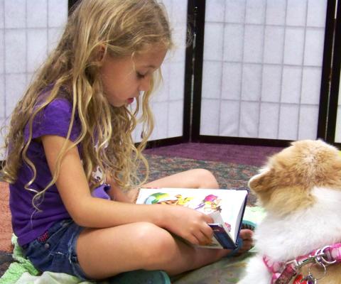 Girl reading to a therapy dog.  