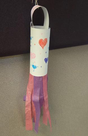 White tube with pink and purple streamers hanging from the bottom. The tube is decorated with red, pink and purple hearts