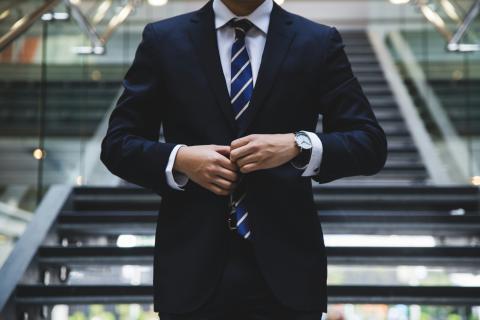 A man in a suit standing in front of stairs.