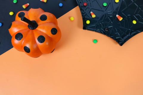 An orange pumpkin with black dots on an orange and black background with a spiderweb plate and candy corn.