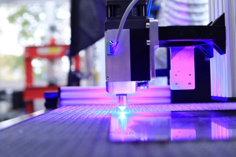 A laser cutter with a purple light shining on it as it cuts