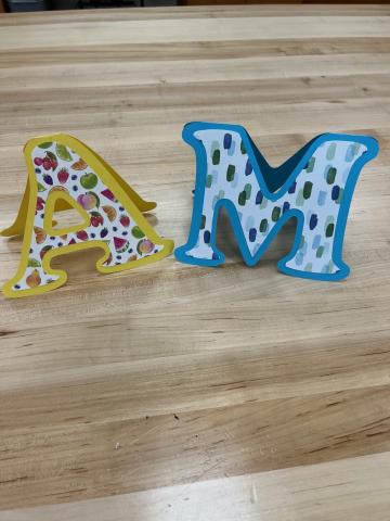 yellow A and blue M cut out of paper and folded into a card