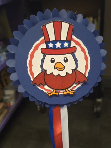 A bald eagle wearing a red, white and blue hat attached to a red, white and blue rosette with red, white and blue ribbon