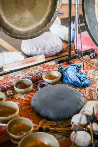 Tibetan singing bowls and sound bath instruments surrounded by a brightly colored rug. Photo by Kitera Dent on Unsplash.