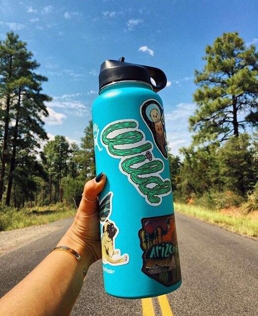 Hands holding a blue water bottle with various vinyl stickers