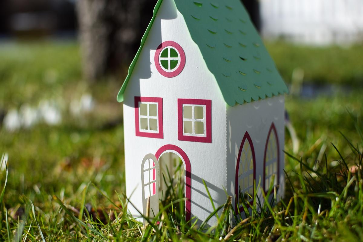 Model house made out of paper sitting in a field of grass