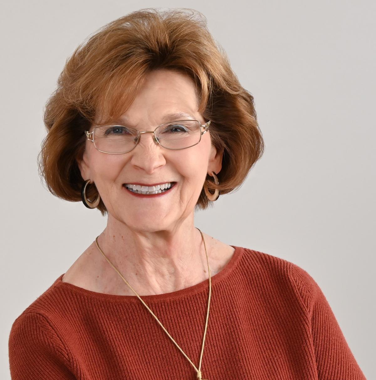 Image of Diana Hoyt, white woman with short red hair and glasses in a red top