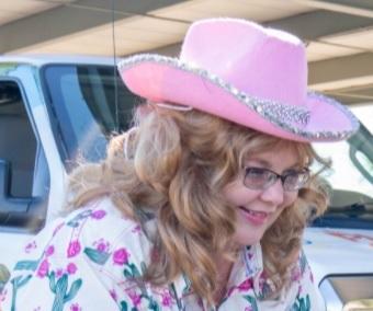 Woman with pink cowboy hat and a shirt with cacti and flowers on it.  