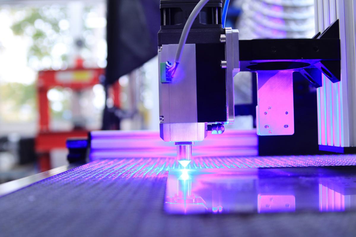 A laser cutter with a purple light shining on it as it cuts