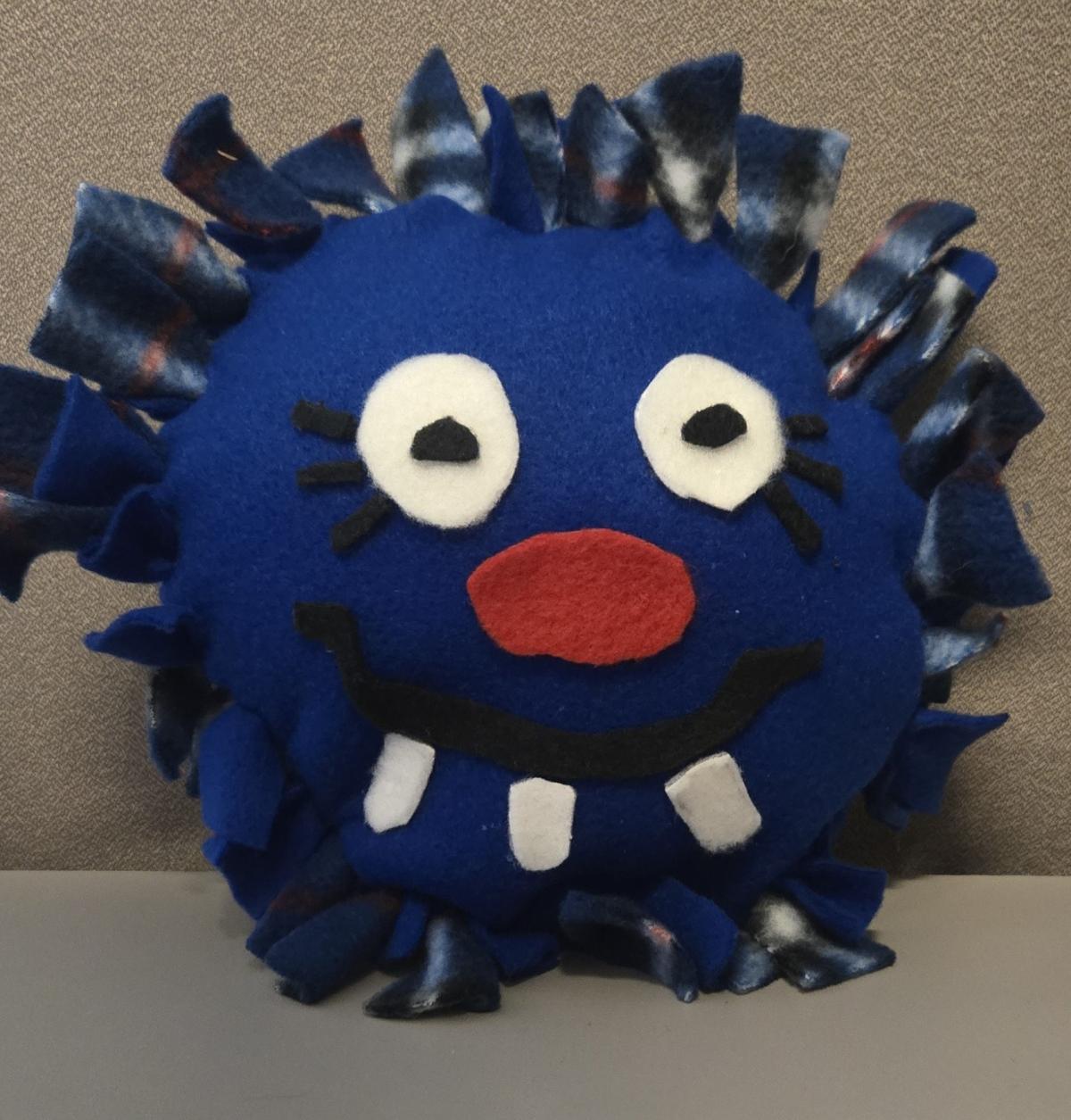 Blue pillow with blue plaid fringe with white eyes, red nose, and a crooked mouth
