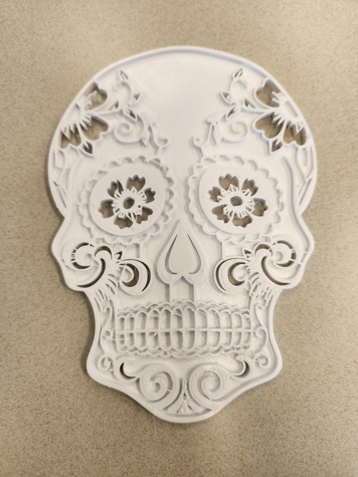 A white 3D printed flat sugar skull with raised embellishments