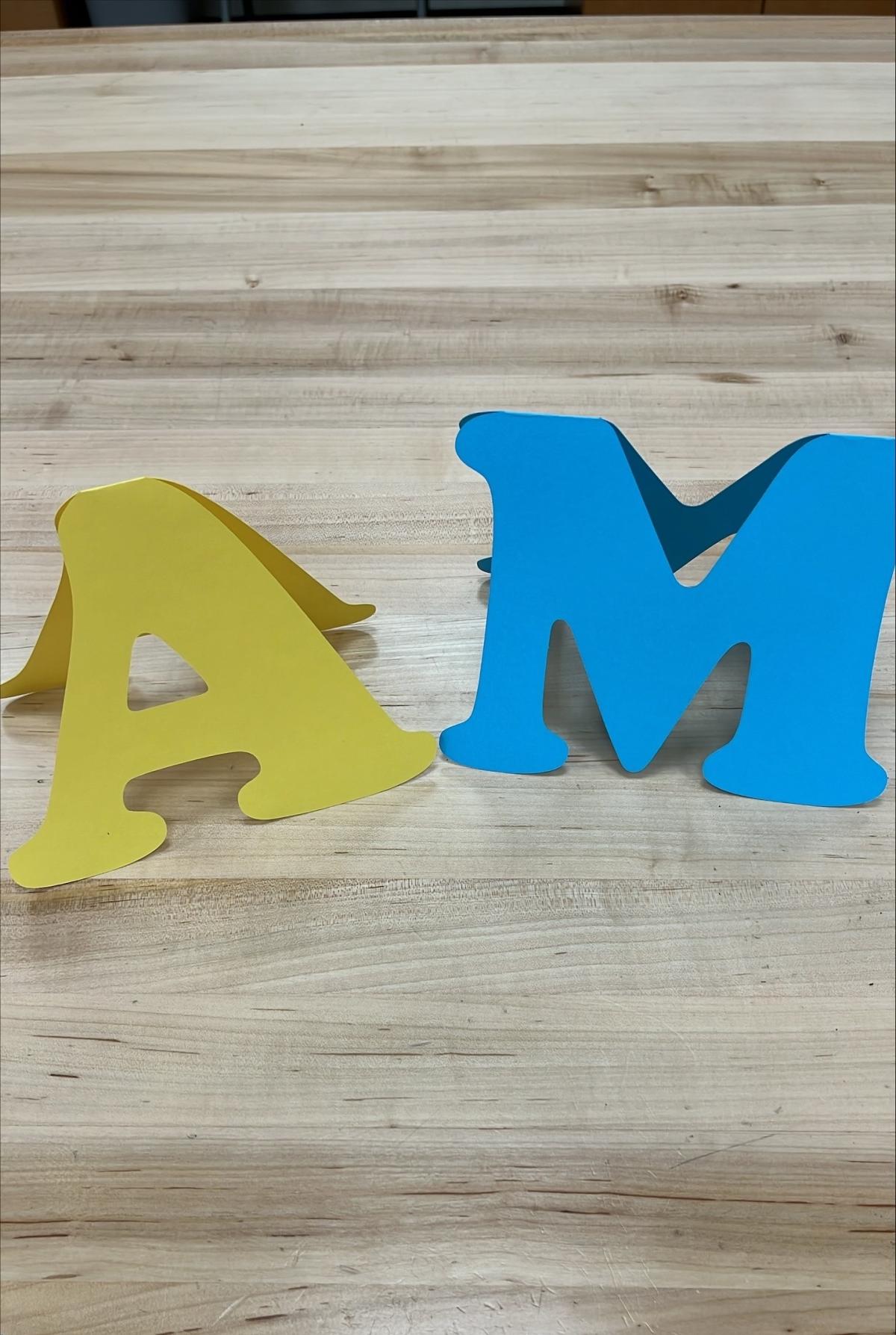 yellow A and blue M cut out of paper and folded into a card